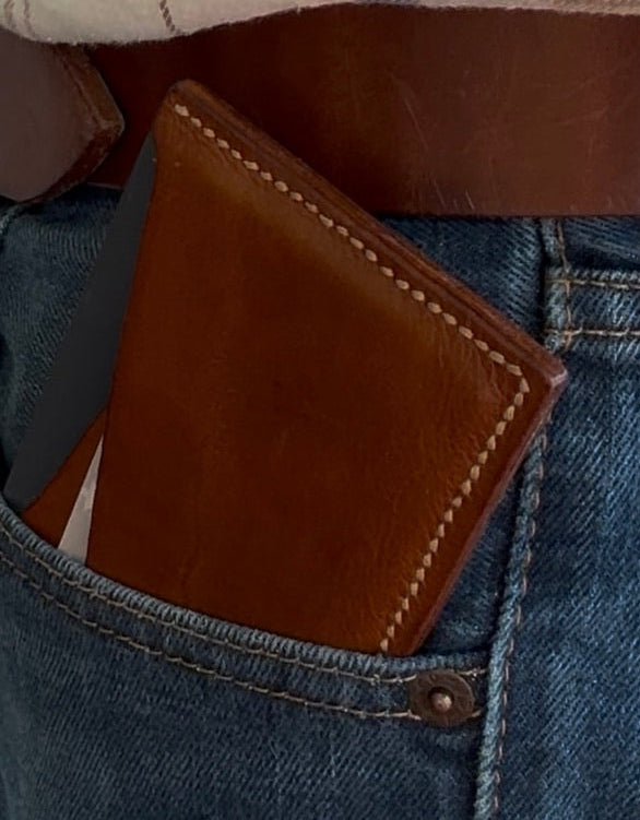 Brown leather wallet in a pocket with plaid shirt and jeans in the background